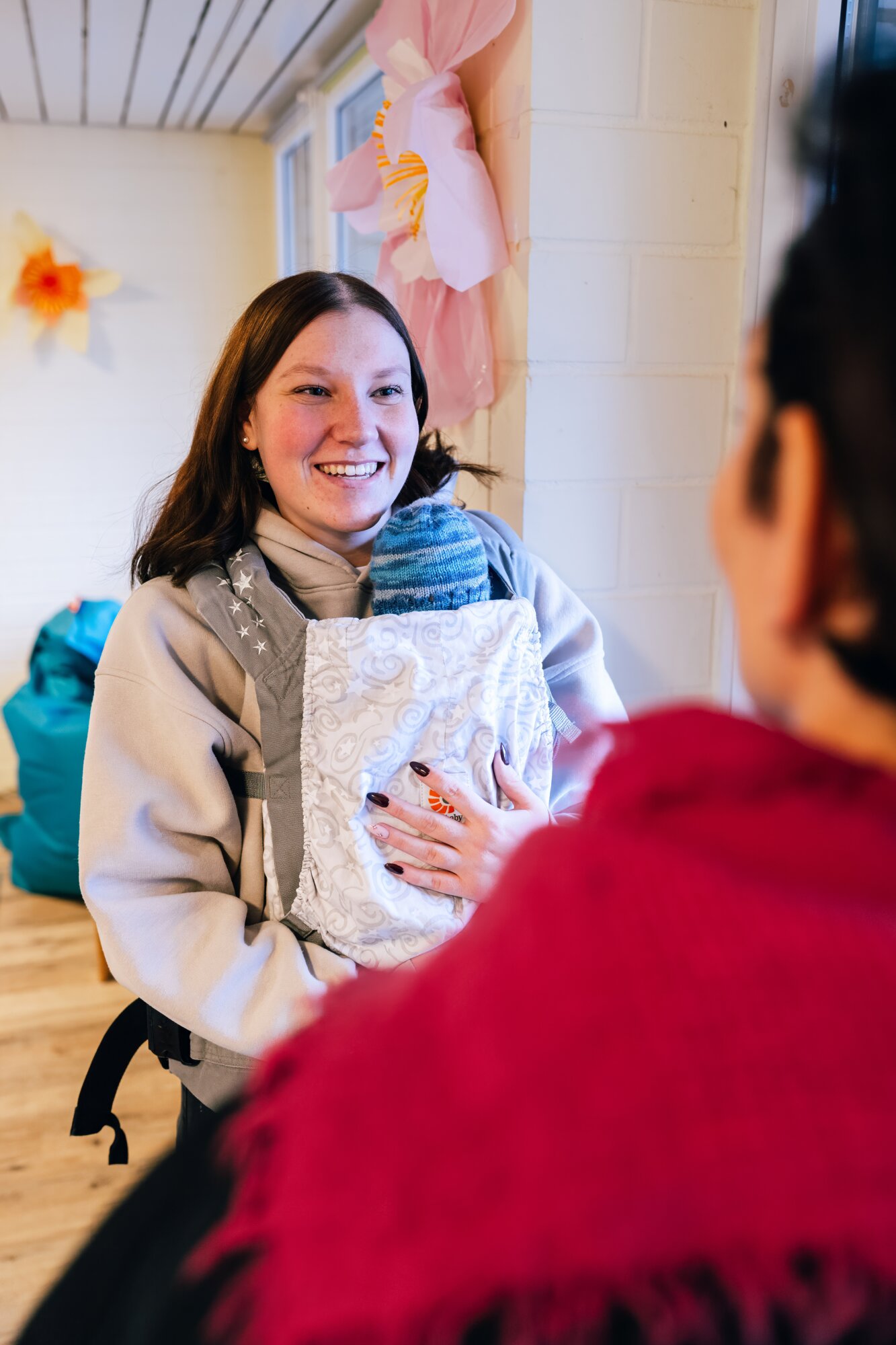 Junge Mutter mit Baby in der Trage im Gespräch in der Mutter/Vater-Kind-Wohngruppe